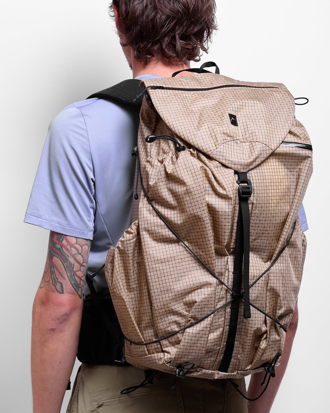 A person wearing a beige, grid-patterned backpack with multiple compartments and shoulder straps.