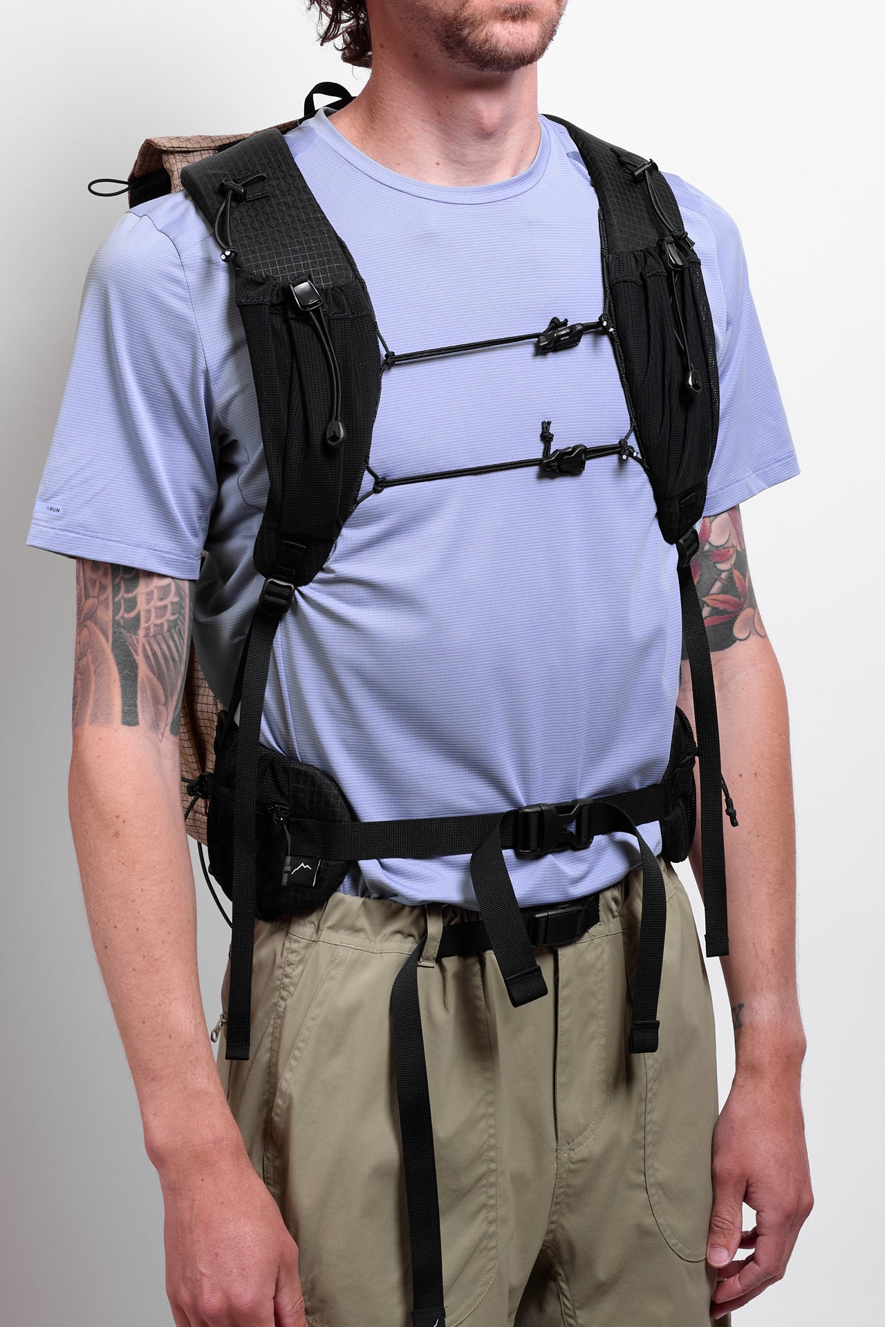 A person wearing a beige, grid-patterned backpack with multiple compartments and shoulder straps.